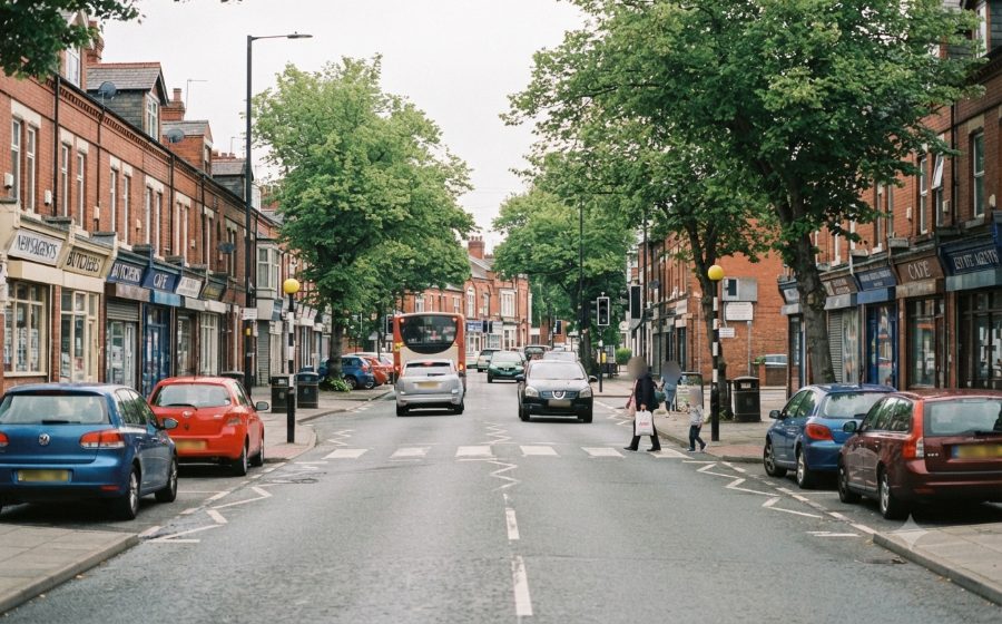 Palatine Road in Northenden village: red-brick shop parades, parked cars on both sides and a bus in the traffic